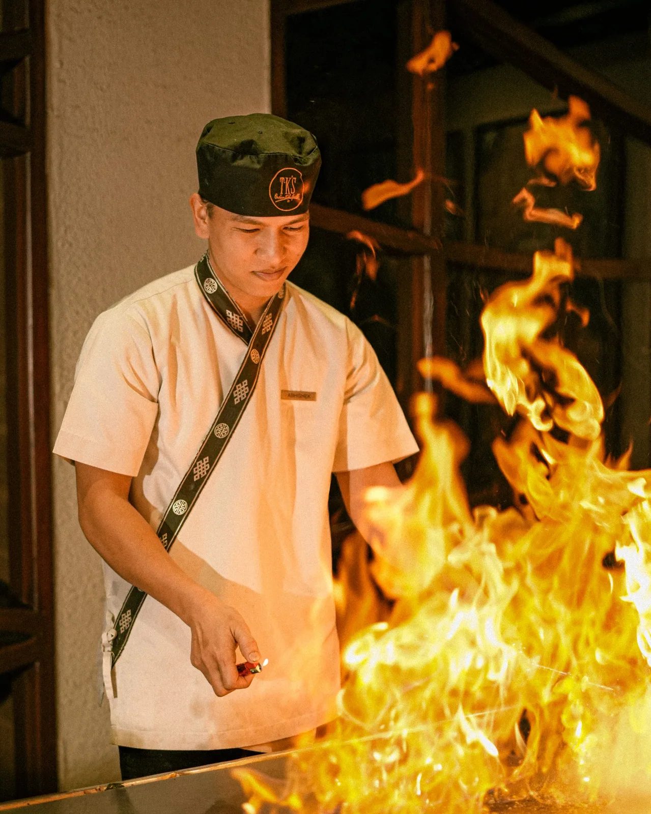 A chef behind a tall wall of flame on the grill