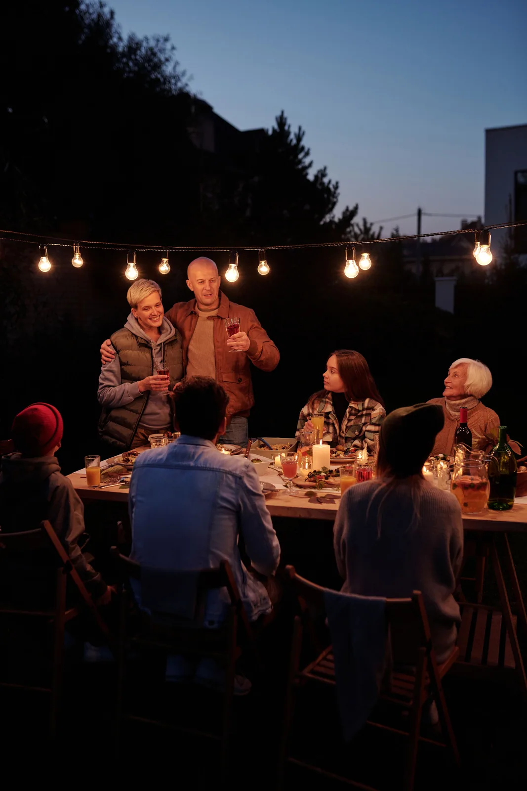 A long table of guests dining outdoors at night beneath overhead lights