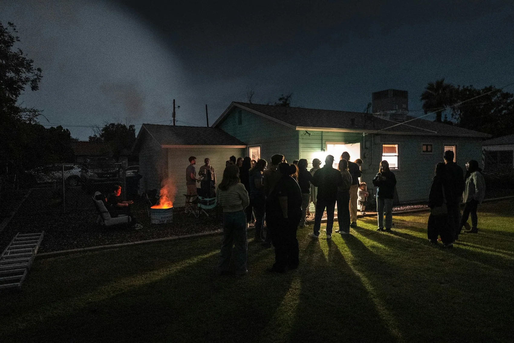 A back garden full of people talking around a fire after dark