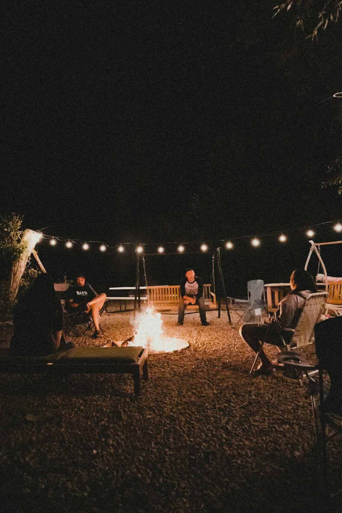 Guests gathered around a lit fire pit at dusk with lanterns strung overhead
