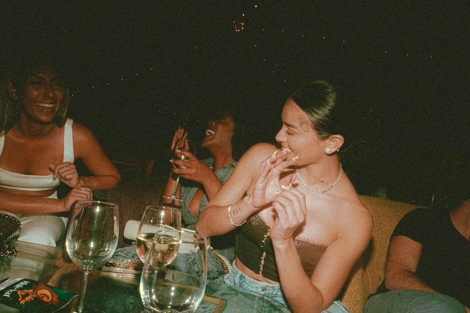 Three friends laughing together at an outdoor table late in the evening