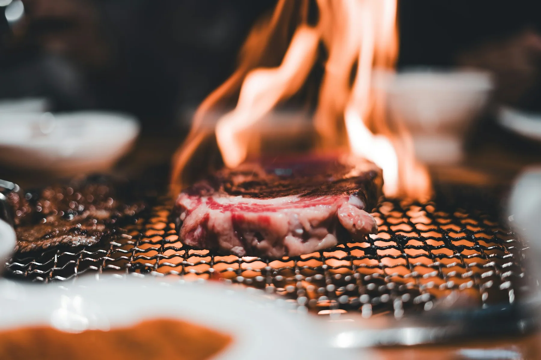 A steak searing over open flame on the grill, smoke rising around it