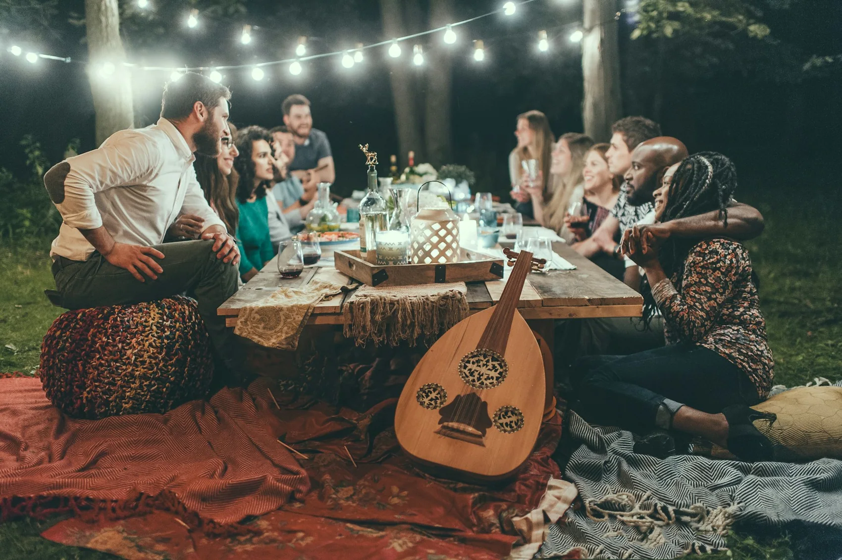 A long table of guests eating together under a canopy of string lights after dark