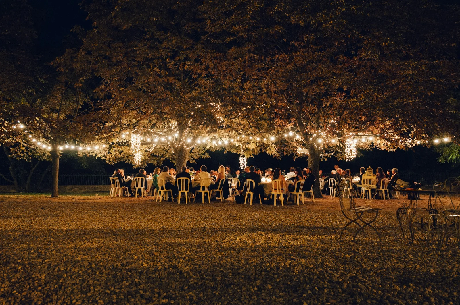 A long outdoor dinner table under a canopy of string lights in a garden after dark