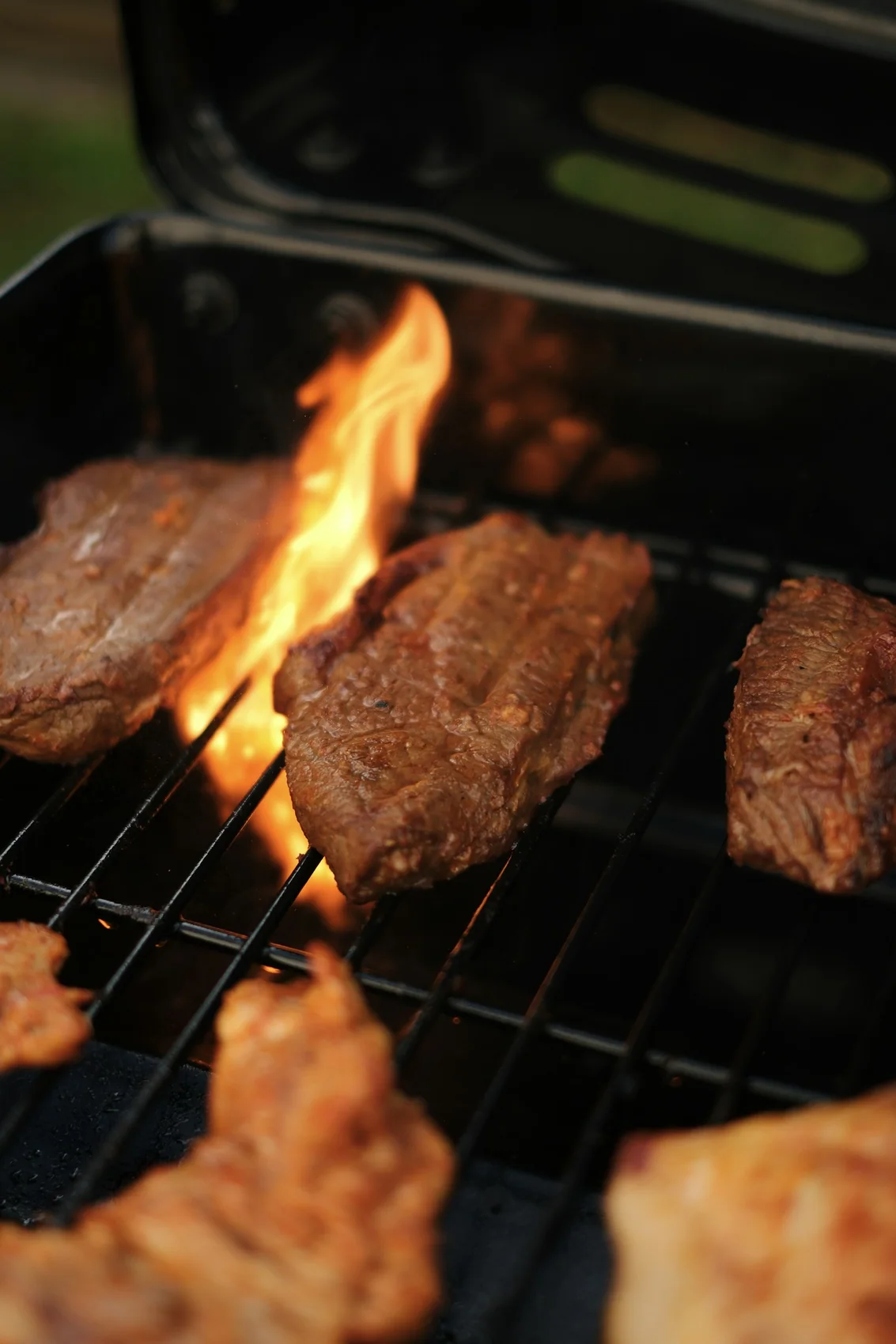 A steak resting on the grill with smoke drifting across warm background lights