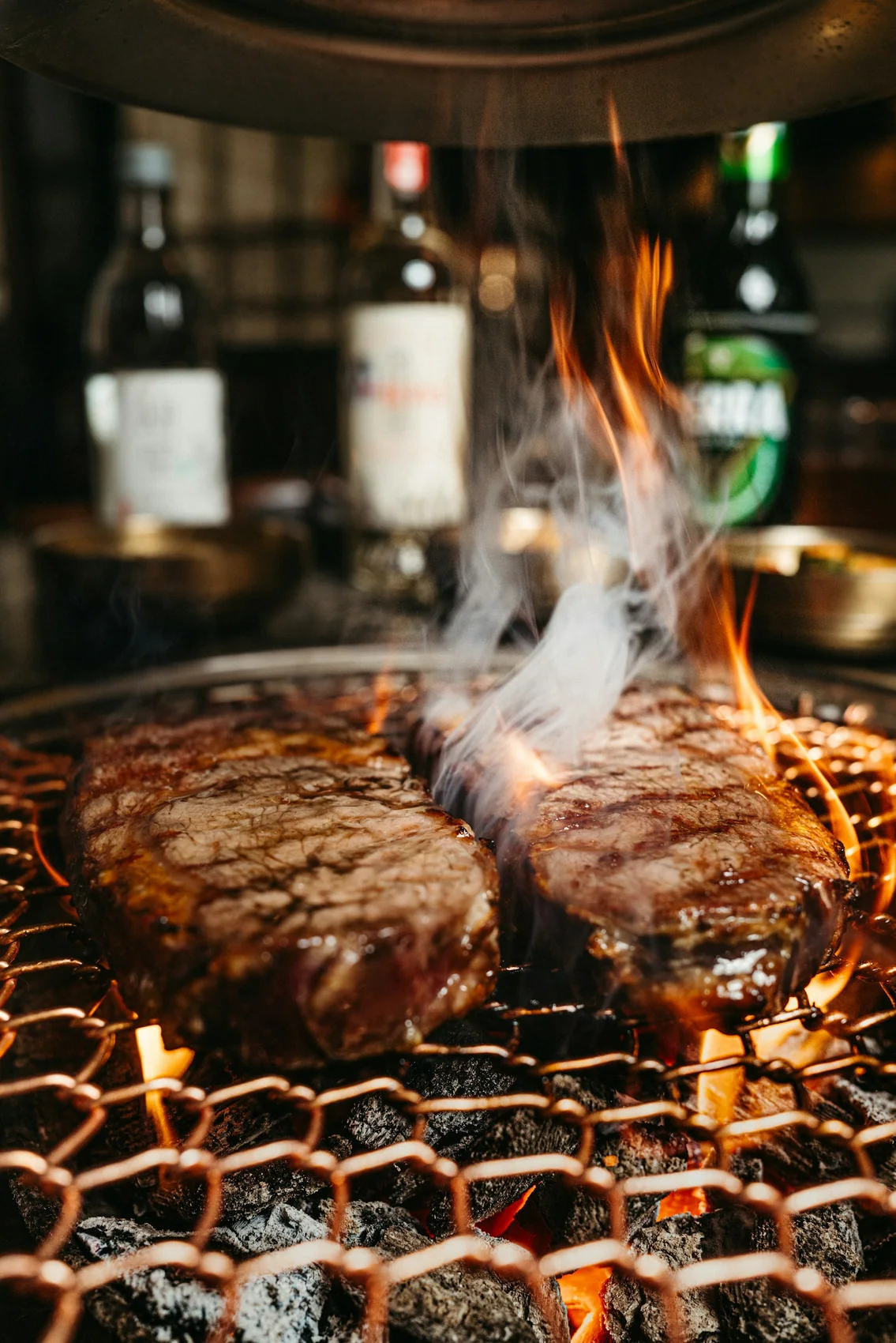 Steaks cooking over open flame with smoke rising around them