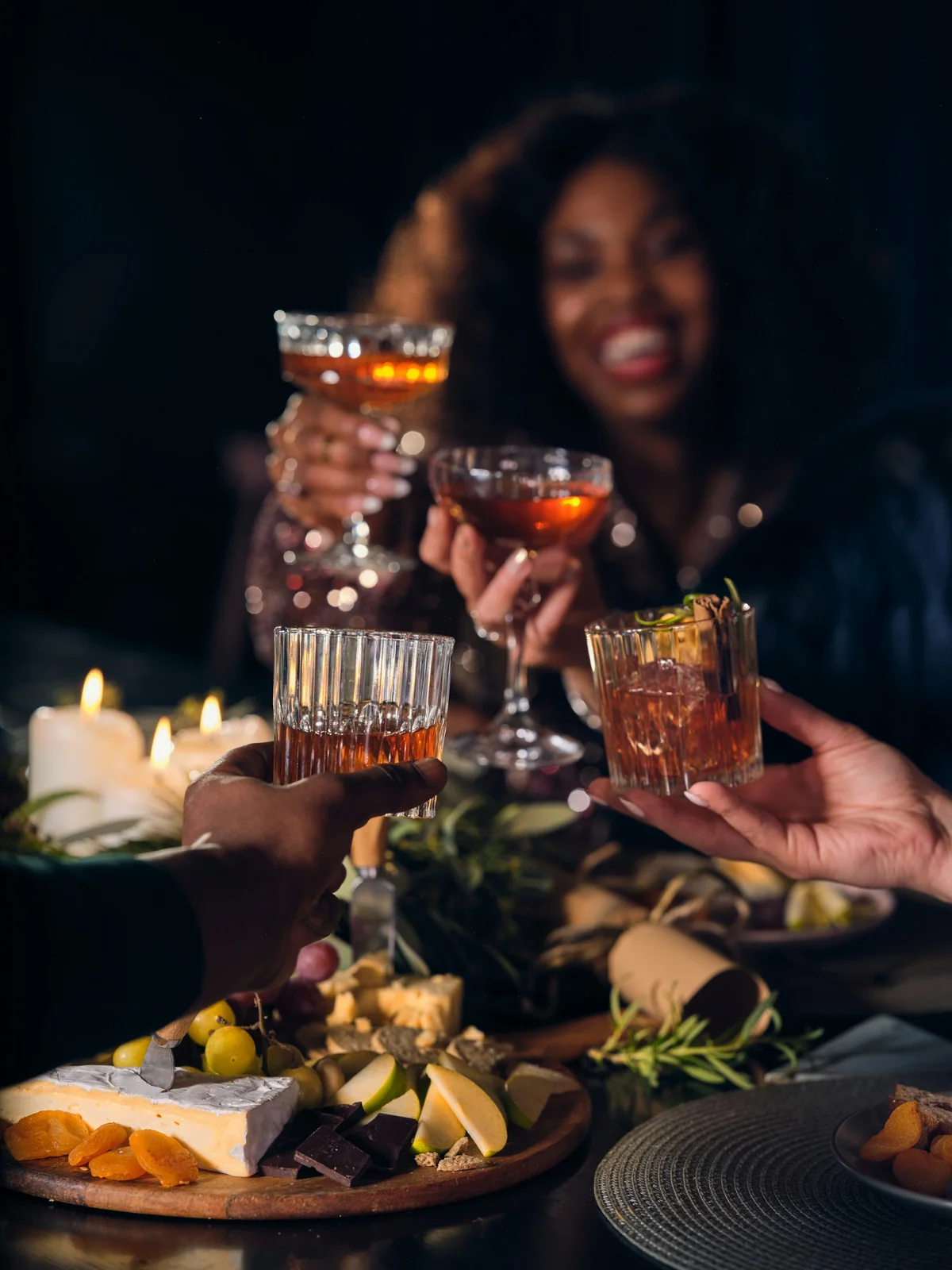 Hands meeting over the middle of a table to clink glasses above a spread of food