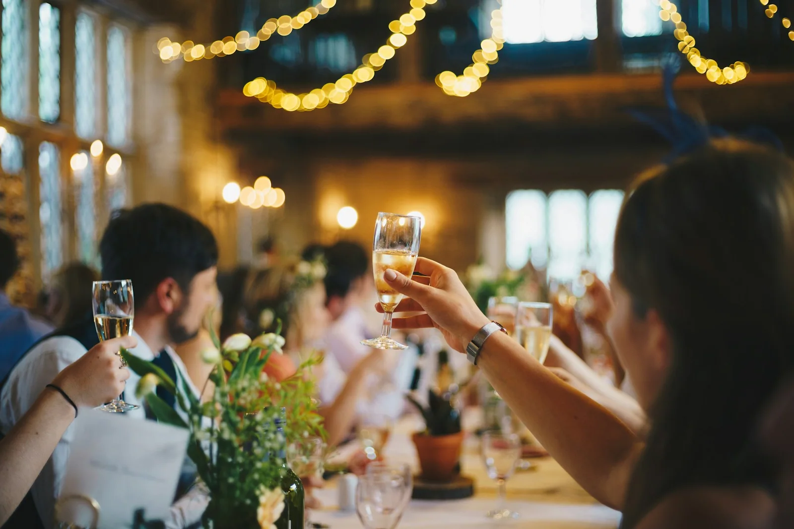 Guests raising their glasses together beneath warm hanging lights