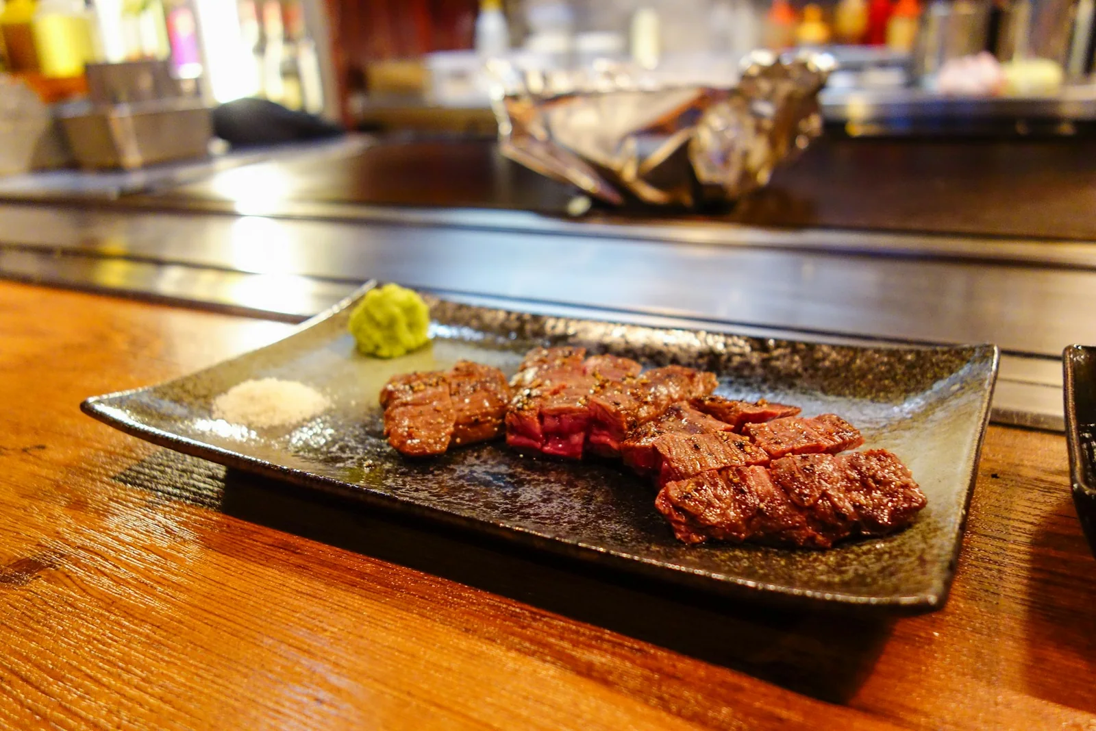 Sliced grilled beef plated with wasabi and salt beside the teppanyaki counter